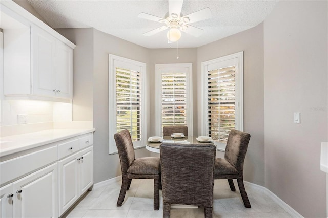 dining room with a textured ceiling, light tile patterned floors, baseboards, and ceiling fan