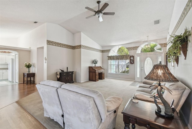 living area with visible vents, ceiling fan, vaulted ceiling, light wood-style floors, and a textured ceiling