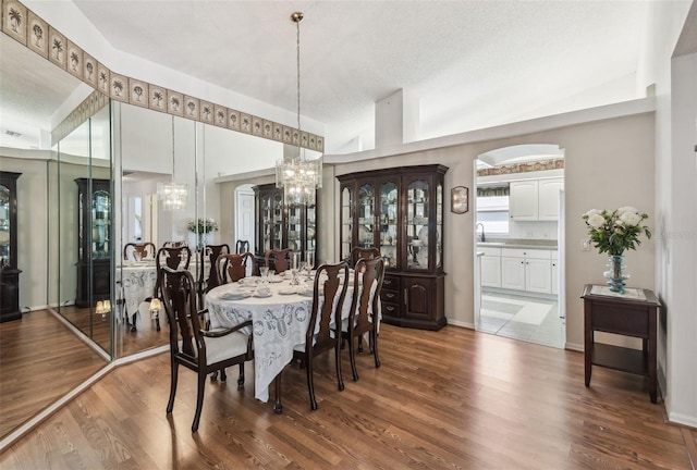 dining space with vaulted ceiling, a notable chandelier, wood finished floors, and arched walkways