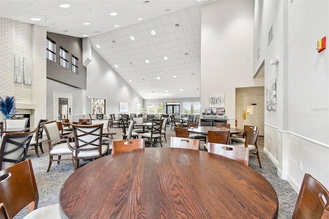 dining space featuring visible vents, carpet, baseboards, a brick fireplace, and a towering ceiling