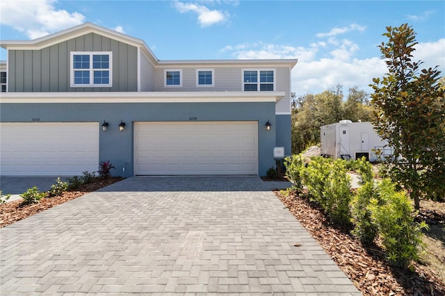 view of front of home with decorative driveway, board and batten siding, an attached garage, and stucco siding