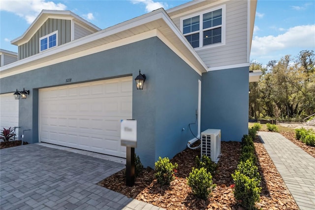 view of home's exterior with board and batten siding, ac unit, stucco siding, driveway, and an attached garage