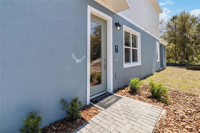 view of exterior entry with stucco siding and a lawn