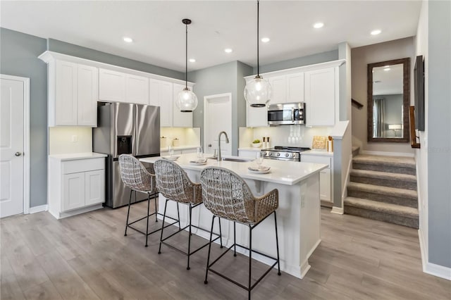 kitchen with an island with sink, a sink, stainless steel appliances, a breakfast bar area, and light wood finished floors