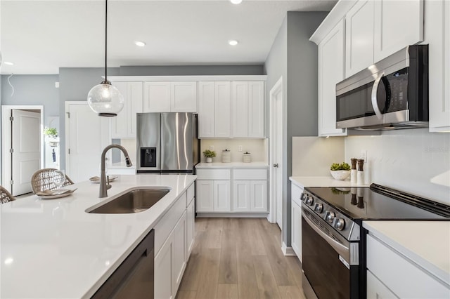 kitchen featuring a sink, white cabinetry, stainless steel appliances, light wood-style floors, and light countertops