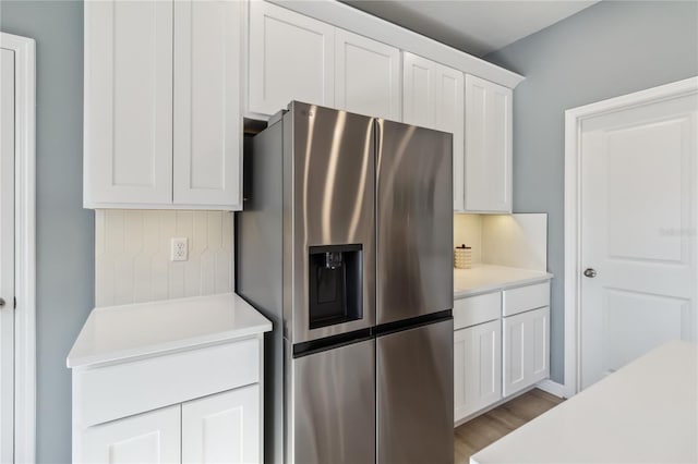 kitchen with light wood finished floors, white cabinets, stainless steel fridge with ice dispenser, and light countertops