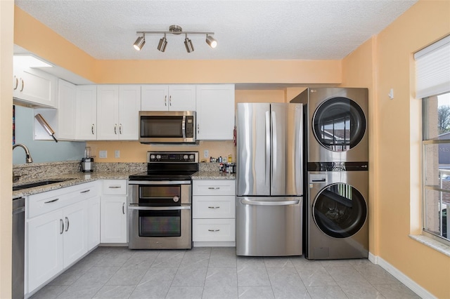 kitchen with stacked washer and clothes dryer, white cabinetry, appliances with stainless steel finishes, and a sink