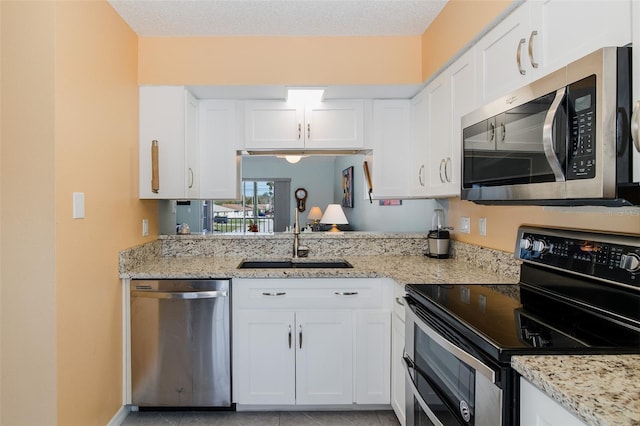 kitchen featuring white cabinets, appliances with stainless steel finishes, light stone countertops, and a sink