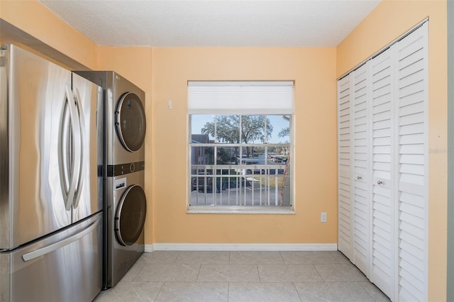 washroom featuring light tile patterned floors, stacked washer / drying machine, a textured ceiling, and laundry area