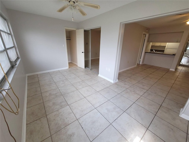 unfurnished bedroom with light tile patterned floors, ceiling fan, a closet, and baseboards