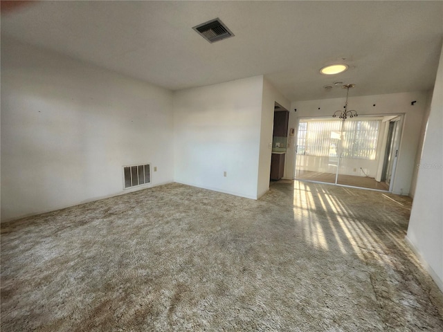 carpeted empty room with visible vents and an inviting chandelier