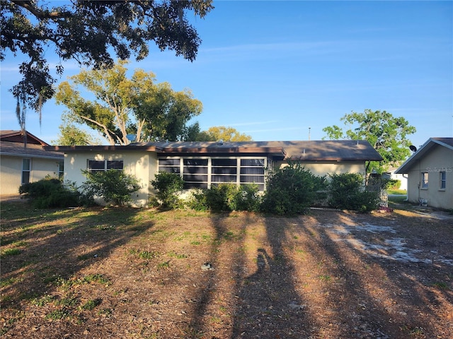 back of house with dirt driveway and stucco siding