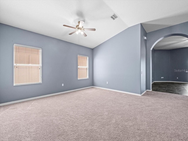 carpeted spare room with visible vents, baseboards, lofted ceiling, arched walkways, and ceiling fan