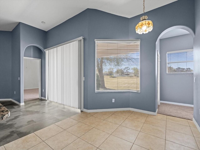 spare room featuring light tile patterned floors, baseboards, and arched walkways