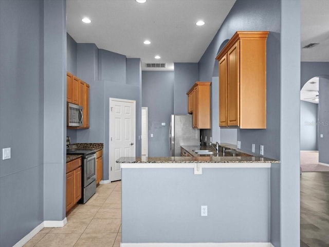 kitchen featuring a sink, stainless steel appliances, dark stone counters, a peninsula, and light tile patterned flooring