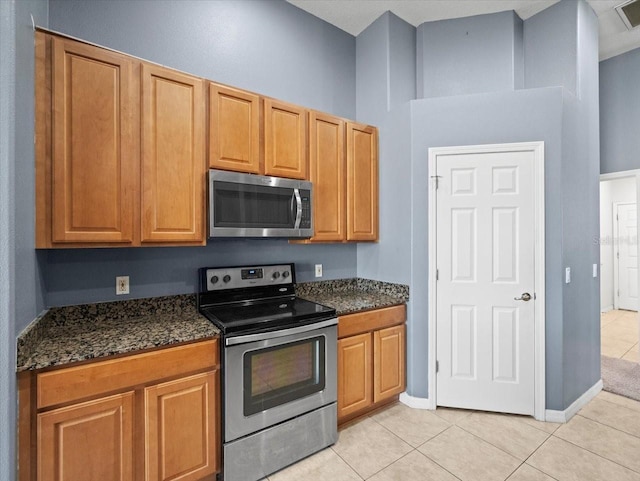 kitchen featuring visible vents, dark stone countertops, stainless steel appliances, light tile patterned floors, and baseboards