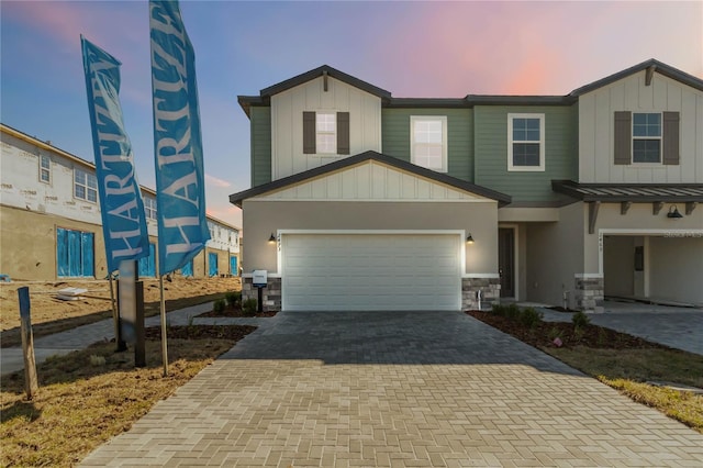 view of front of house featuring decorative driveway, stone siding, and board and batten siding