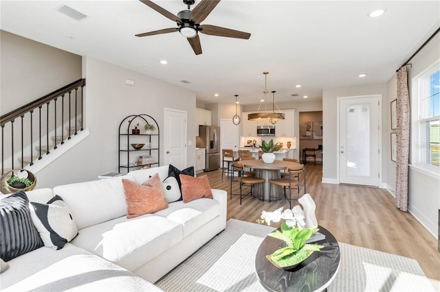 living room featuring light wood finished floors, visible vents, recessed lighting, and stairs