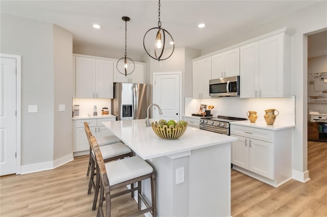 kitchen featuring a breakfast bar area, a kitchen island with sink, hanging light fixtures, light countertops, and appliances with stainless steel finishes