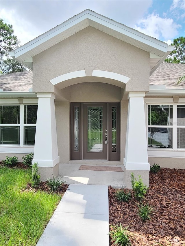 view of exterior entry featuring stucco siding and a shingled roof