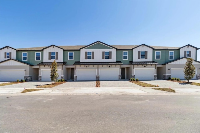 townhome / multi-family property with driveway, a standing seam roof, a garage, stone siding, and metal roof