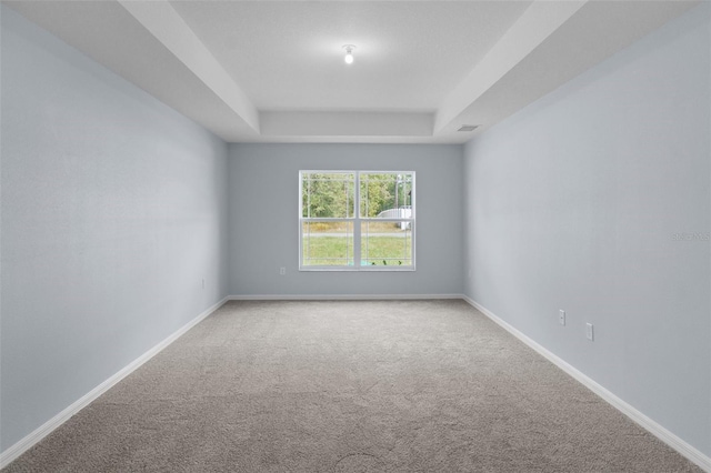 empty room with a tray ceiling, baseboards, visible vents, and carpet flooring