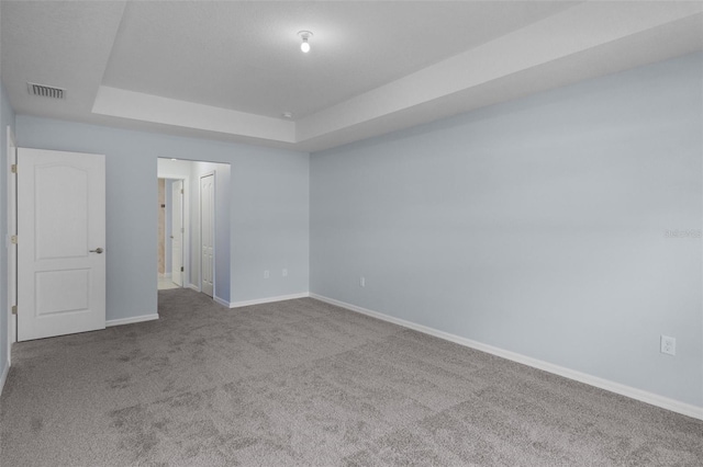 spare room with visible vents, carpet flooring, a raised ceiling, and baseboards