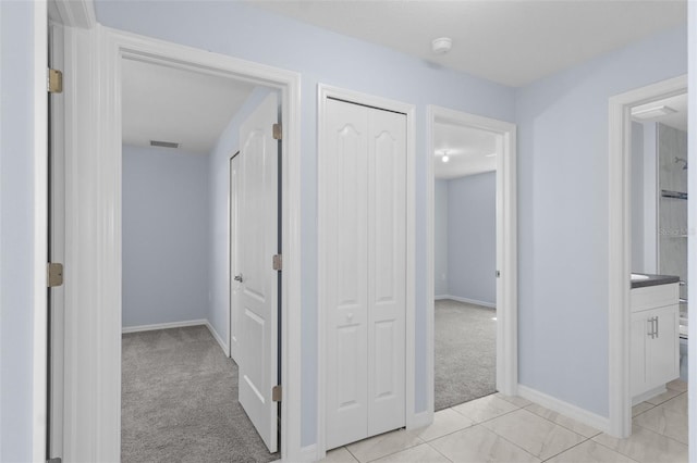 corridor with light carpet, visible vents, baseboards, and light tile patterned flooring