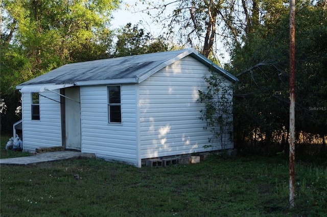 view of side of property with an outbuilding, a yard, and roof with shingles