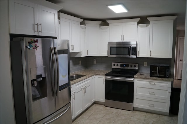 kitchen with white cabinets, light stone counters, tasteful backsplash, and appliances with stainless steel finishes