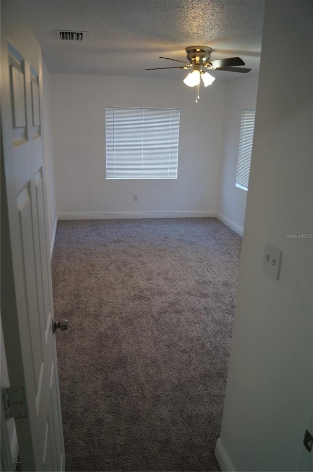 empty room featuring visible vents, baseboards, ceiling fan, carpet flooring, and a textured ceiling