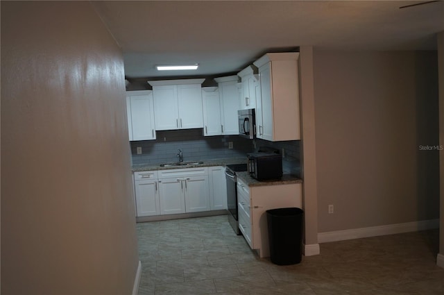 kitchen with light stone countertops, stainless steel appliances, a sink, white cabinetry, and backsplash