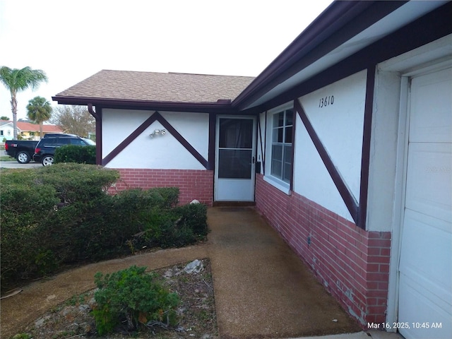 view of exterior entry with a shingled roof, brick siding, and stucco siding