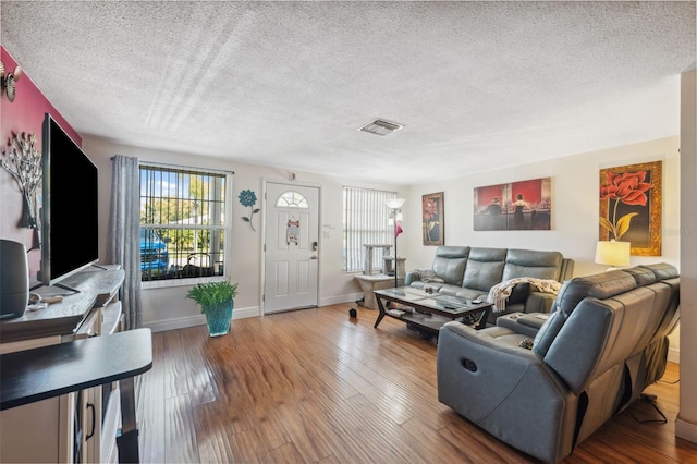 living room featuring visible vents, a textured ceiling, baseboards, and wood finished floors