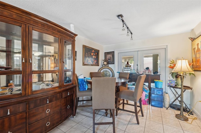 dining room with track lighting, a textured ceiling, french doors, light tile patterned flooring, and baseboards