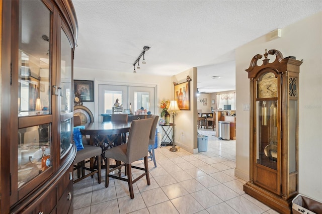 dining area featuring baseboards, french doors, rail lighting, light tile patterned flooring, and a textured ceiling