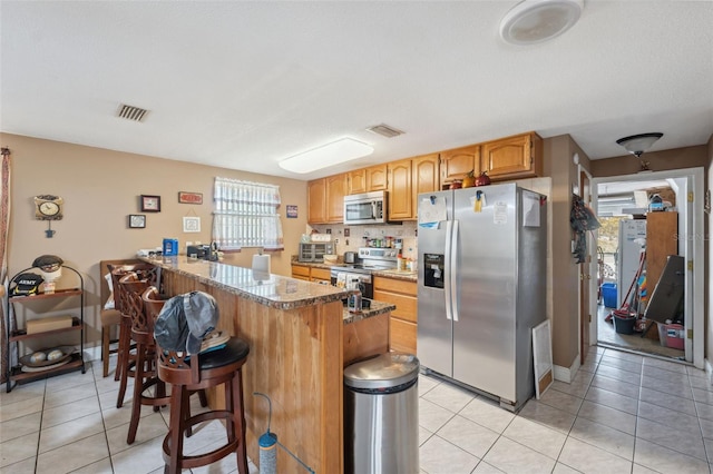 kitchen with visible vents, appliances with stainless steel finishes, a peninsula, and light tile patterned flooring