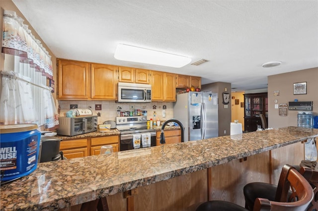 kitchen featuring a breakfast bar area, visible vents, a toaster, appliances with stainless steel finishes, and backsplash