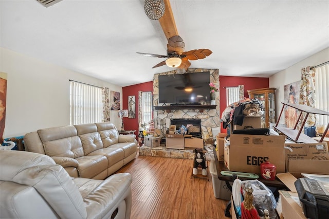 living room with a stone fireplace, vaulted ceiling with beams, wood finished floors, and a ceiling fan