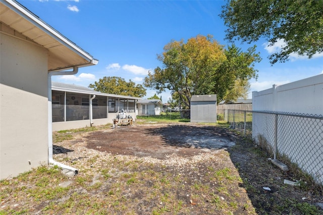 view of yard featuring a storage shed, an outdoor structure, fence, and a sunroom