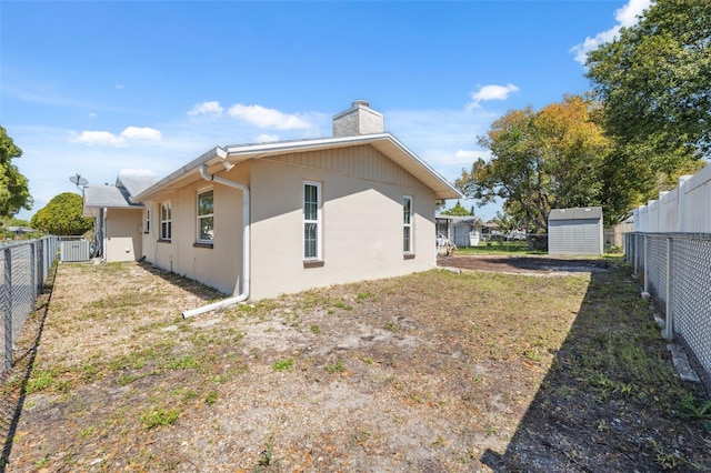 back of house with a fenced backyard, a chimney, stucco siding, an outdoor structure, and a storage unit