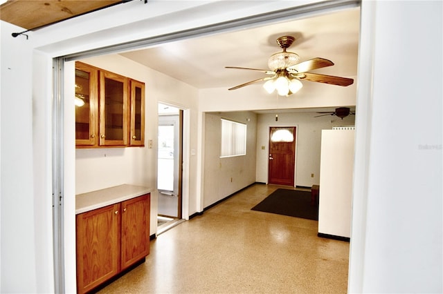 kitchen with brown cabinets, a ceiling fan, fridge, light countertops, and glass insert cabinets