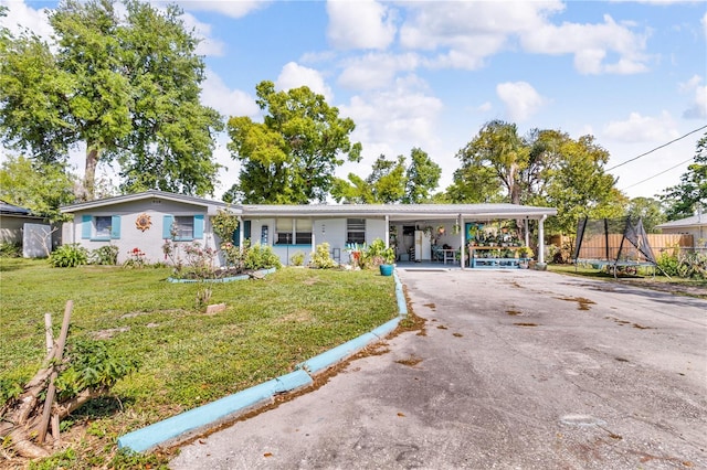 ranch-style house with an attached carport, a front lawn, a trampoline, and driveway