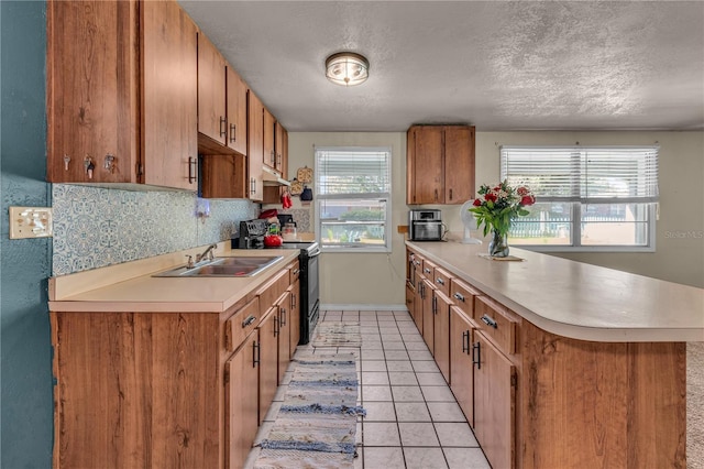 kitchen featuring tasteful backsplash, black range with electric cooktop, light countertops, a peninsula, and a sink