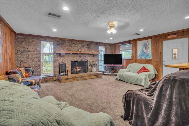 living area with visible vents, carpet, a brick fireplace, and wood walls