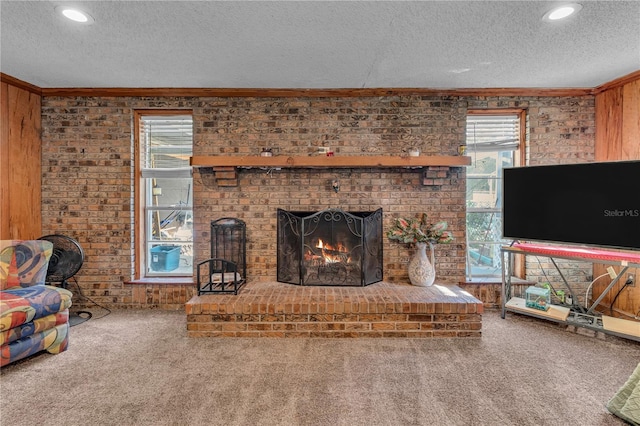 living area featuring wooden walls, a brick fireplace, carpet, ornamental molding, and a textured ceiling