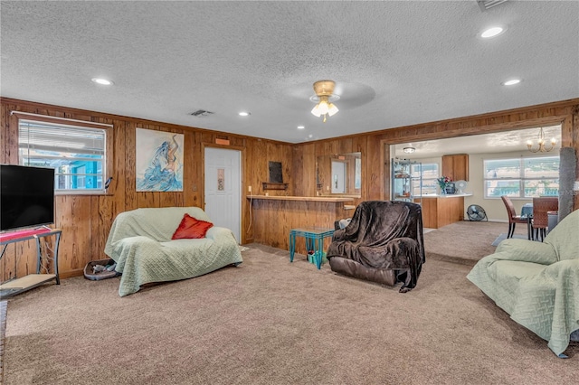 carpeted living room with visible vents, wooden walls, and a textured ceiling