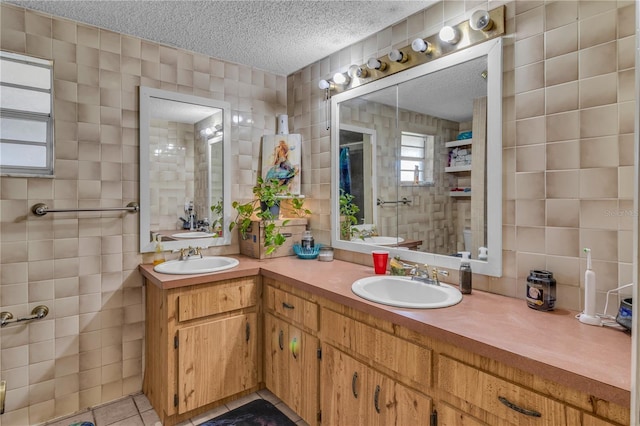 full bath with a sink, a textured ceiling, tile walls, and double vanity