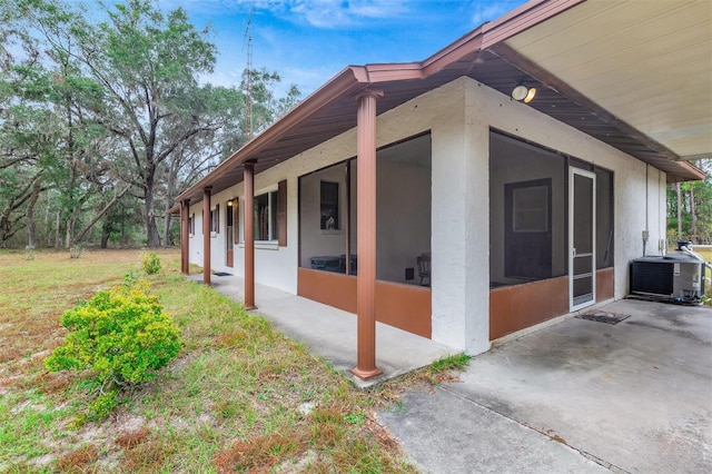 view of property exterior featuring a yard, central AC unit, stucco siding, and a sunroom