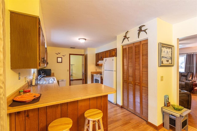 kitchen with a sink, light countertops, white appliances, light wood-style floors, and a peninsula